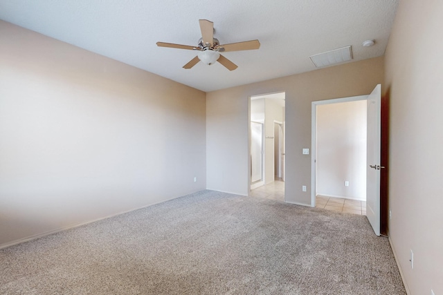 spare room featuring ceiling fan, light tile patterned flooring, visible vents, and light colored carpet