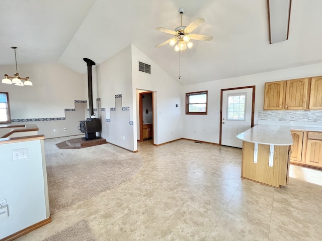 kitchen with light brown cabinets, high vaulted ceiling, a center island, a wood stove, and hanging light fixtures