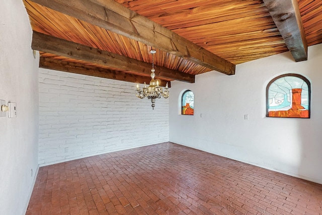 spare room featuring a notable chandelier, beam ceiling, wooden ceiling, and brick wall