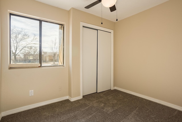 unfurnished bedroom with ceiling fan, a closet, and dark carpet