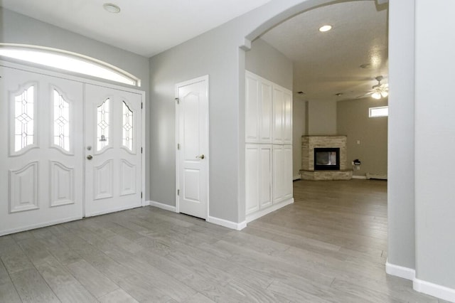 foyer entrance with baseboard heating, ceiling fan, a fireplace, and light wood-type flooring