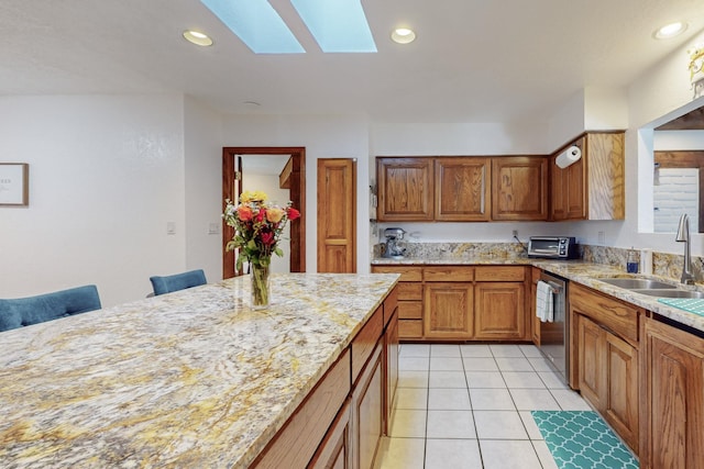 kitchen featuring sink, stainless steel dishwasher, a skylight, light stone countertops, and a breakfast bar