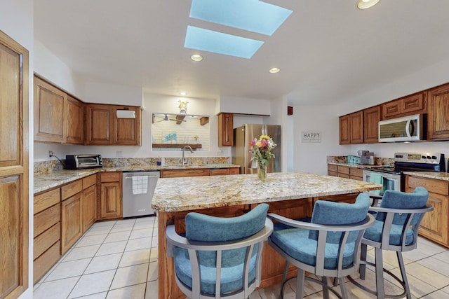 kitchen with stainless steel appliances, a kitchen island, a skylight, and light tile patterned floors