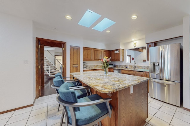 kitchen featuring sink, a center island, light tile patterned floors, a skylight, and appliances with stainless steel finishes