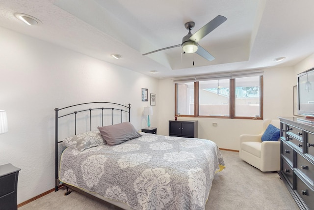 carpeted bedroom with ceiling fan and a raised ceiling