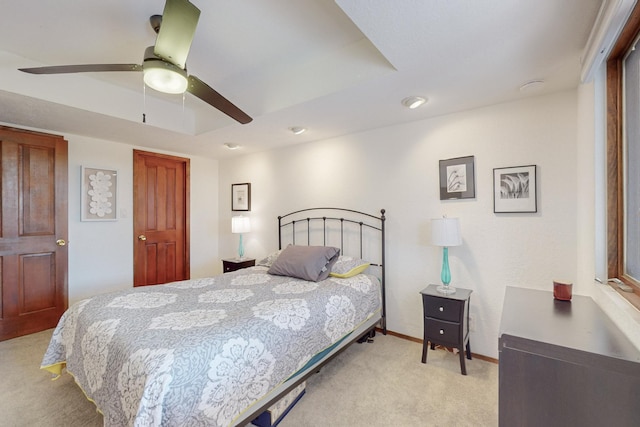 bedroom featuring ceiling fan, light colored carpet, and a tray ceiling