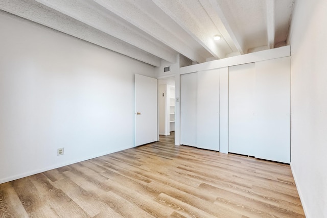 unfurnished bedroom featuring a closet, light hardwood / wood-style flooring, beamed ceiling, and a textured ceiling