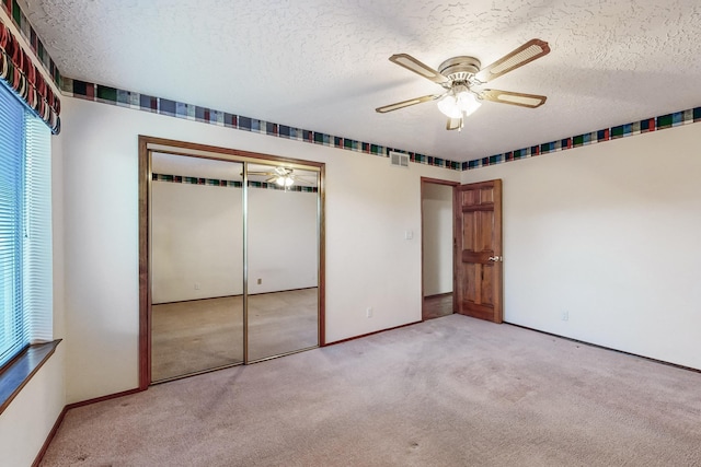 unfurnished bedroom with light carpet, ceiling fan, a closet, and a textured ceiling