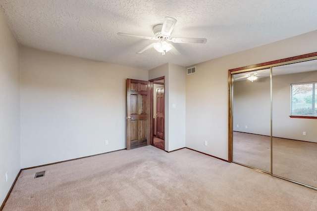 unfurnished bedroom with ceiling fan, light carpet, a textured ceiling, and a closet