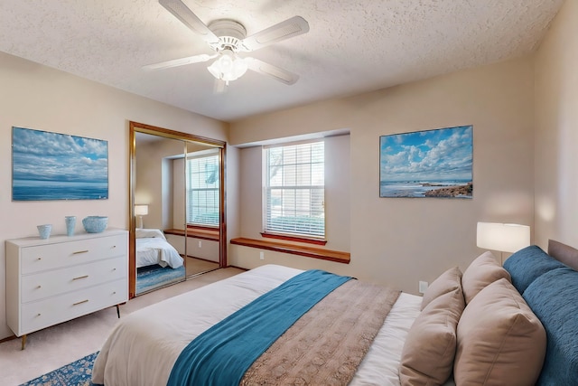 bedroom featuring ceiling fan, light colored carpet, a closet, and a textured ceiling