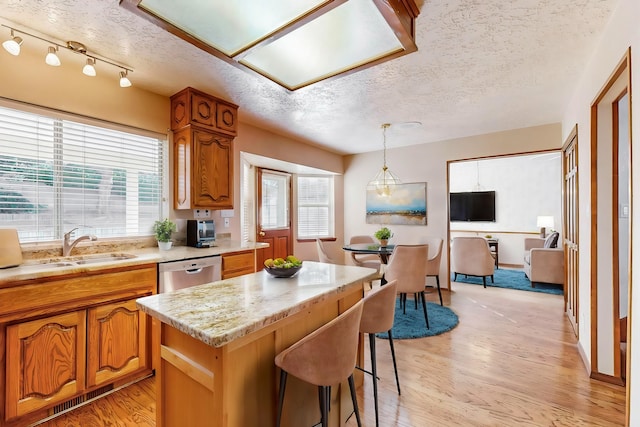 kitchen featuring decorative light fixtures, sink, a center island, stainless steel dishwasher, and light hardwood / wood-style flooring