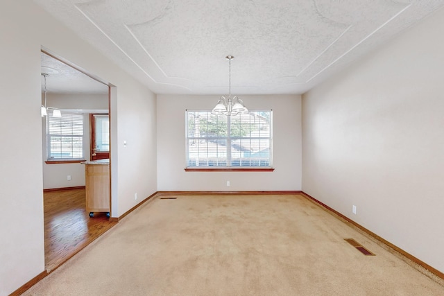 carpeted spare room featuring a notable chandelier and a textured ceiling