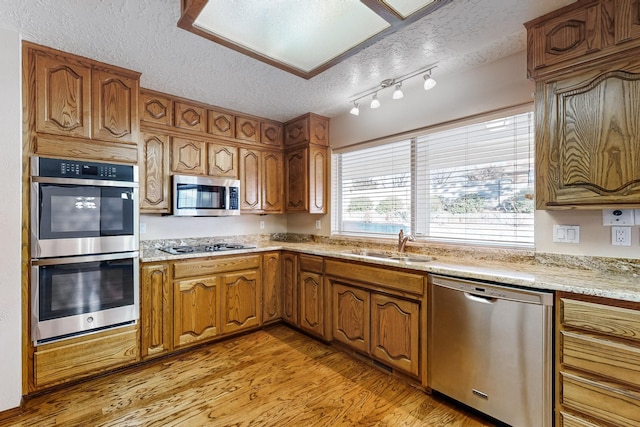 kitchen with sink, a textured ceiling, stainless steel appliances, light stone countertops, and light hardwood / wood-style floors