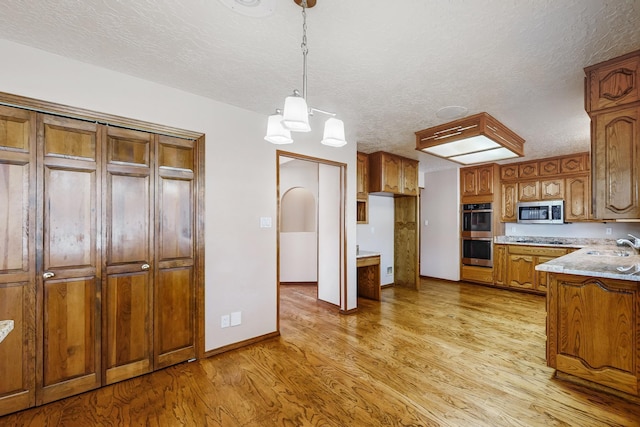 kitchen featuring decorative light fixtures, light stone counters, stainless steel appliances, a textured ceiling, and light hardwood / wood-style flooring