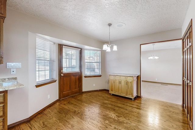 unfurnished dining area with an inviting chandelier, hardwood / wood-style flooring, and a textured ceiling