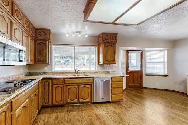 kitchen with appliances with stainless steel finishes, sink, light hardwood / wood-style flooring, and a textured ceiling