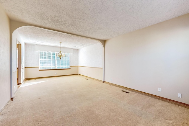 spare room with carpet flooring, an inviting chandelier, and a textured ceiling