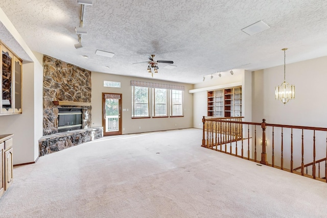 carpeted living room with rail lighting, a stone fireplace, ceiling fan with notable chandelier, and a textured ceiling