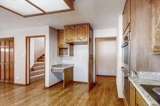 kitchen with light hardwood / wood-style flooring, light stone countertops, a textured ceiling, black electric cooktop, and stainless steel double oven