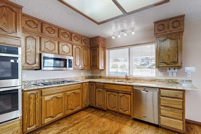 kitchen featuring sink, appliances with stainless steel finishes, light stone counters, a textured ceiling, and light wood-type flooring