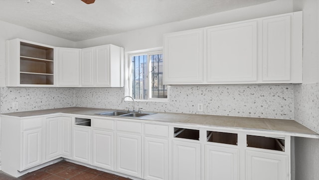 kitchen featuring backsplash, sink, dark tile patterned floors, a textured ceiling, and white cabinetry