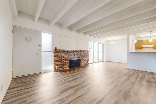 unfurnished living room with hardwood / wood-style floors, an inviting chandelier, a brick fireplace, and beam ceiling