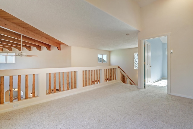 unfurnished room featuring carpet flooring, ceiling fan, and beamed ceiling