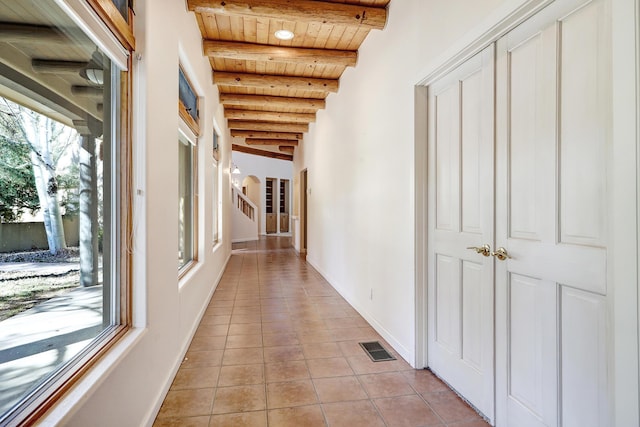 corridor with beam ceiling, plenty of natural light, light tile patterned flooring, and wooden ceiling