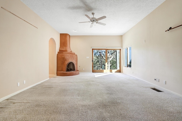 unfurnished living room featuring carpet flooring, ceiling fan, a fireplace, and a textured ceiling