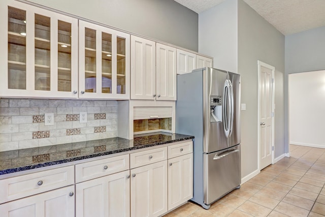 kitchen with white cabinetry, stainless steel fridge with ice dispenser, dark stone counters, a textured ceiling, and light tile patterned floors