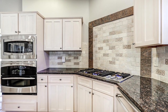 kitchen with white cabinets, appliances with stainless steel finishes, backsplash, and dark stone counters