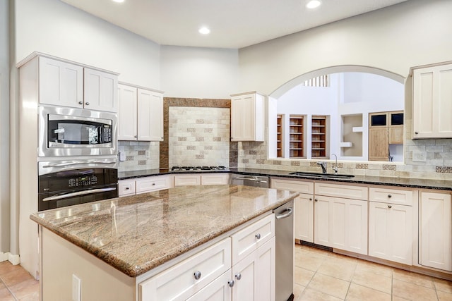 kitchen featuring a center island, sink, light stone countertops, light tile patterned floors, and stainless steel appliances