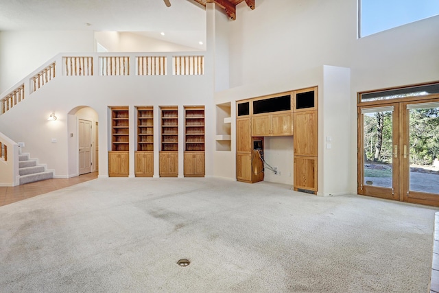 unfurnished living room with light carpet, a high ceiling, french doors, and beamed ceiling