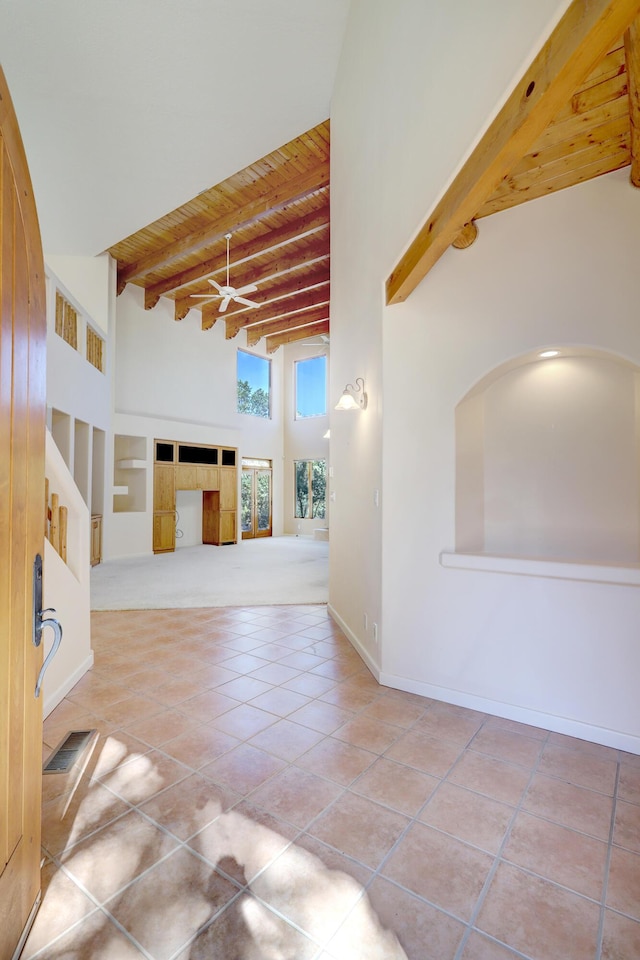 tiled empty room featuring beam ceiling, wood ceiling, and a towering ceiling