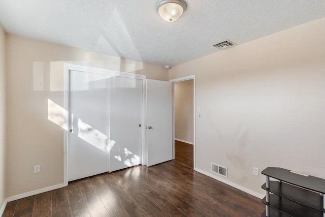 unfurnished bedroom with a textured ceiling, dark hardwood / wood-style floors, and a closet