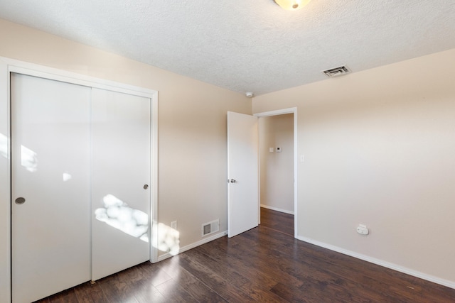 unfurnished bedroom featuring a textured ceiling, dark hardwood / wood-style flooring, and a closet