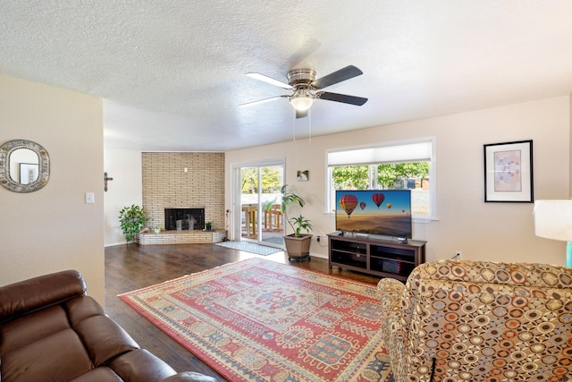 living room featuring ceiling fan, dark hardwood / wood-style flooring, a textured ceiling, and a brick fireplace