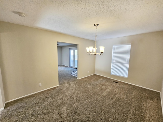 carpeted spare room with a notable chandelier and a textured ceiling