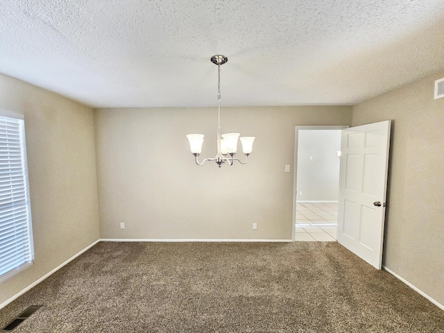 carpeted empty room featuring a textured ceiling and a chandelier