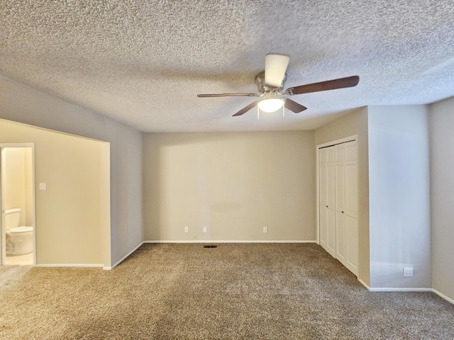 unfurnished bedroom featuring ensuite bath, carpet flooring, ceiling fan, a textured ceiling, and a closet