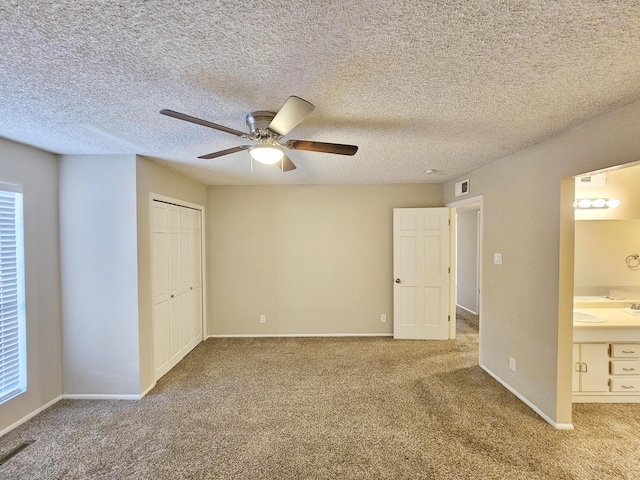 unfurnished bedroom with carpet flooring, ceiling fan, ensuite bathroom, a textured ceiling, and a closet