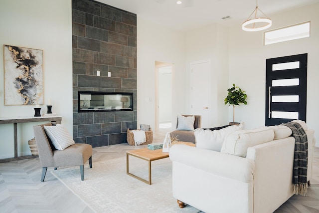 living room with a tiled fireplace, a towering ceiling, and light parquet flooring