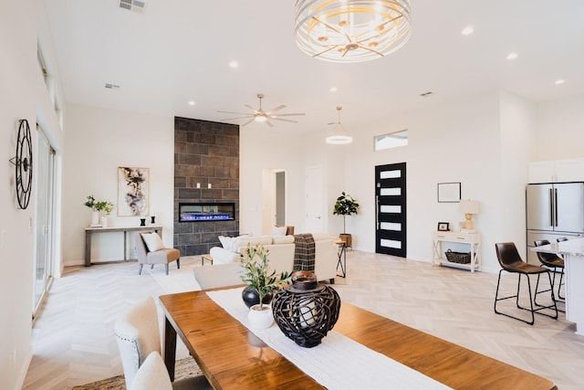 dining space featuring ceiling fan, a towering ceiling, a fireplace, and light parquet flooring