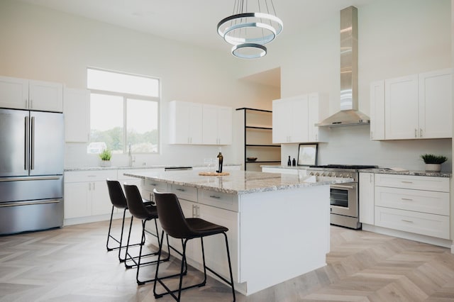 kitchen featuring wall chimney exhaust hood, premium appliances, pendant lighting, white cabinets, and a center island