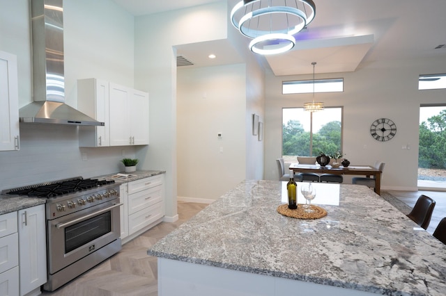 kitchen featuring stainless steel range, wall chimney range hood, white cabinets, a high ceiling, and a center island