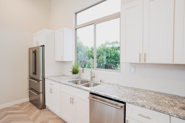 kitchen with light parquet floors, white cabinets, sink, light stone countertops, and stainless steel appliances