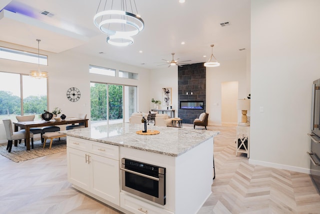 kitchen with pendant lighting, stainless steel oven, white cabinetry, and light parquet flooring