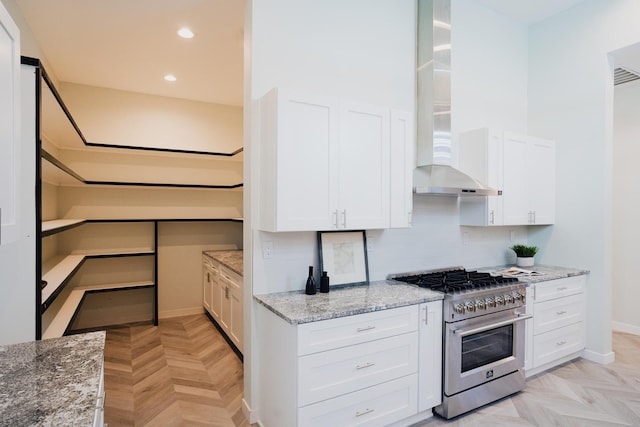 kitchen with high end stove, white cabinets, light stone countertops, and wall chimney exhaust hood