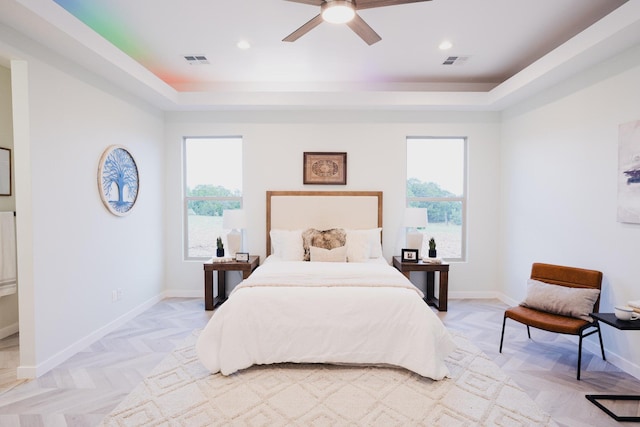 bedroom featuring multiple windows, light parquet flooring, a raised ceiling, and ceiling fan