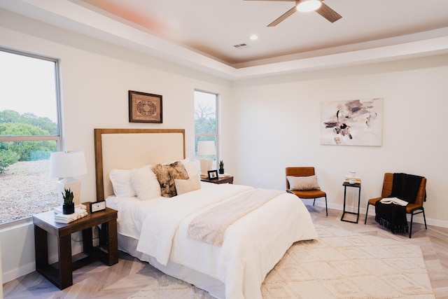 bedroom with light parquet flooring, a tray ceiling, and ceiling fan